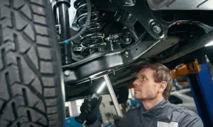 Mechanik bada zawieszenie w samochodzie, oświetlając je latarką. Widać sprężynę i amortyzator.