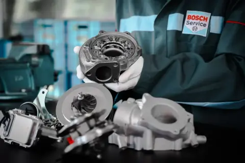 Mechanik w rękawiczkach prezentuje części turbosprężarki. Gotowy do montażu, by zapobiec "blow off" i zapewnić moc.