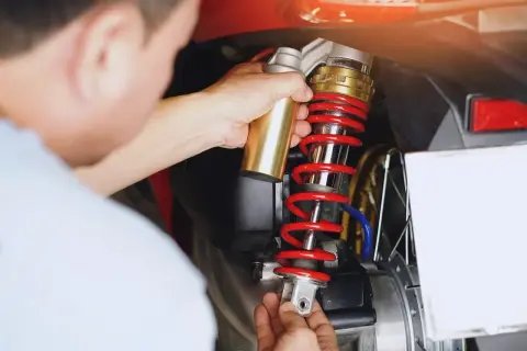 Mechanik sprawdza wylany amortyzator motocykla. Czerwona sprężyna i złote elementy są widoczne.