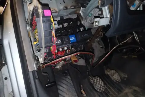 Widok na skrzynkę z bezpiecznikami i przekaźnikami w Audi A4 B6. Widać kolorowe bezpieczniki i wiązki przewodów.