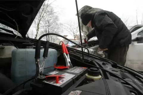 Mężczyzna podłącza kable rozruchowe, by jak szybko naładować akumulator w mroźny dzień.