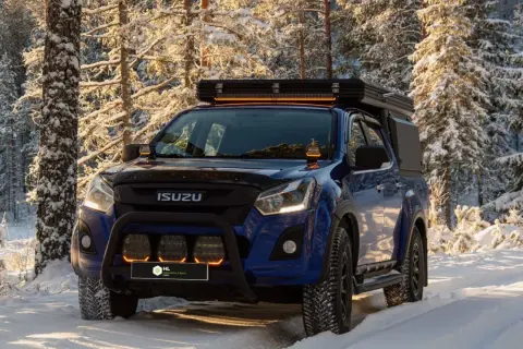 Niebieski Isuzu w zimowym lesie, z dodatkowymi światłami LED na dachu i zderzaku. Dowiedz się, jak ustawić żarówki LED w samochodzie, by podróżować bezpiecznie.