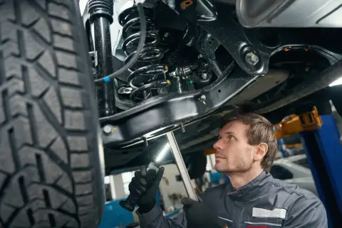 Mechanik bada zawieszenie w samochodzie, oświetlając je latarką. Widać sprężynę i amortyzator.