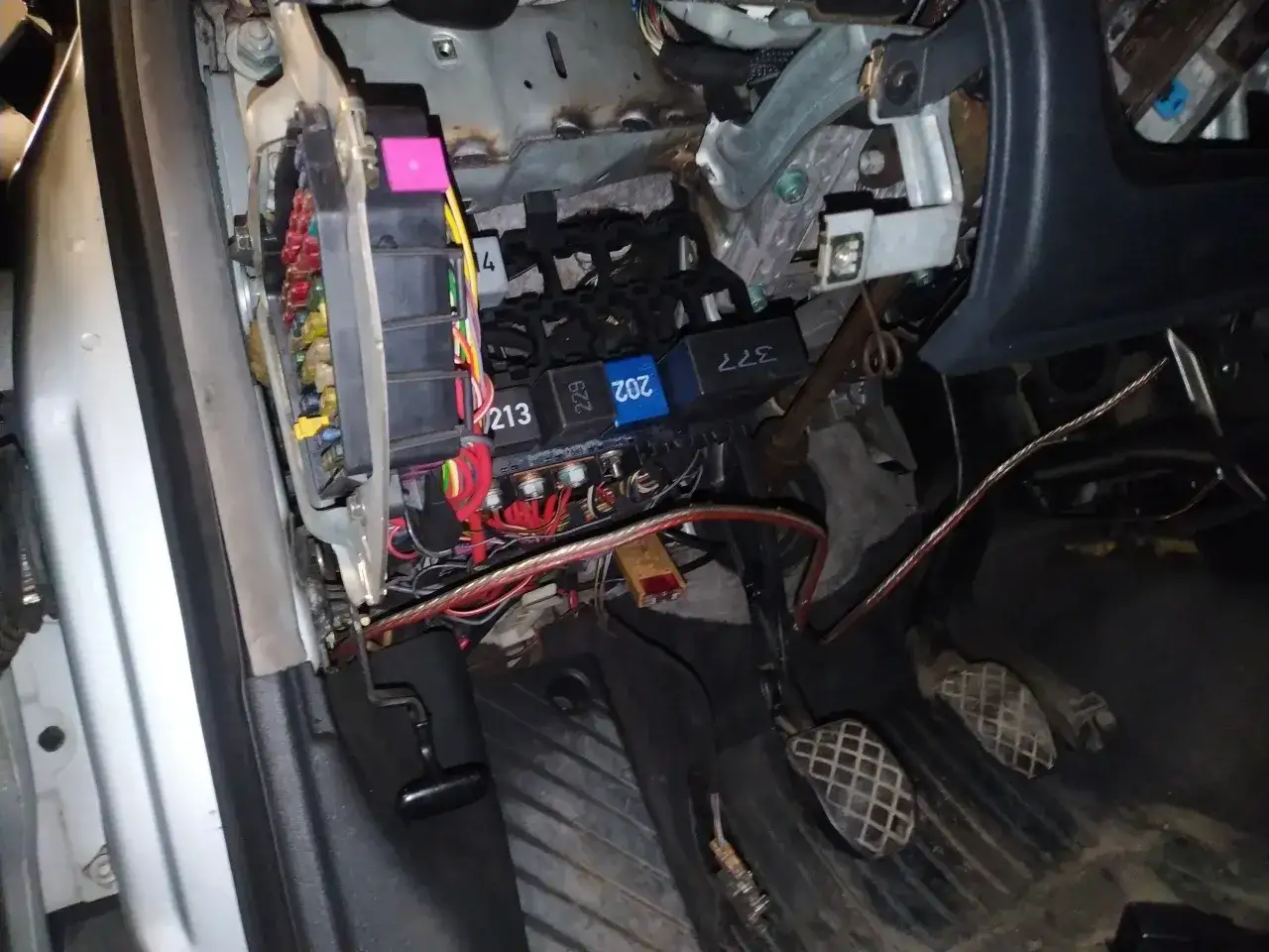 Widok na skrzynkę z bezpiecznikami i przekaźnikami w Audi A4 B5. Widać kolorowe bezpieczniki i kable.