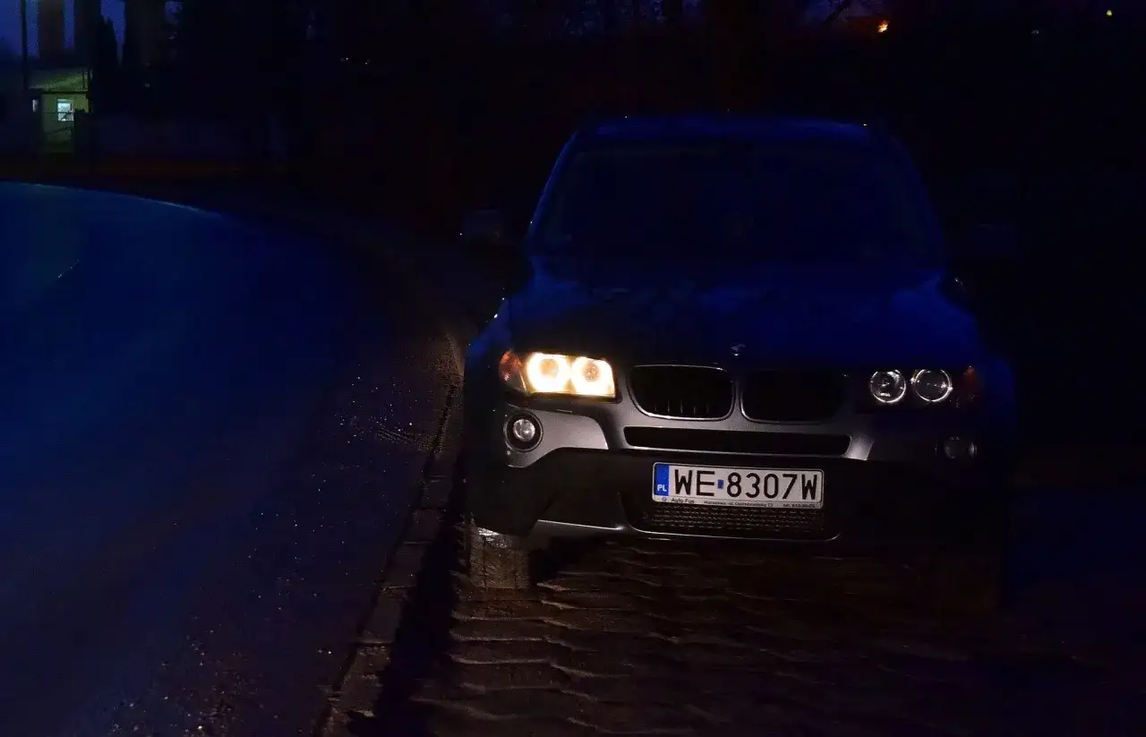 Ciemna noc, mokra droga i zapalone światła postojowe BMW.