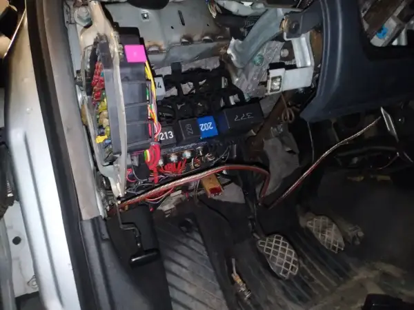 Widok na skrzynkę z bezpiecznikami i przekaźnikami w Audi A4 B6. Widać kolorowe bezpieczniki i wiązki przewodów.